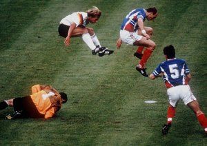 جام جهانی 1990|یورگن کلینزمن از آلمان غربی و پدراگ اسپاسیچ از یوگوسلاوی، از روی دروازه بان، تورورت ایوکویچ، می پرند.