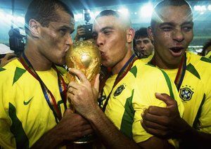 جام جهانی 2002|رونالدو، همراه با ریوالدو و کافو، به جام قهرمانی بوسه می زند. برزیل در فینال جام جهانی 2002 با شکست 2-0 آلمان به مقام قهرمانی رسید. جام جهانی 2002 کره/ژاپن.